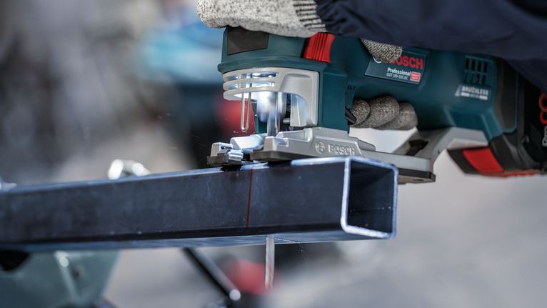 Orang yang mengenakan peralatan keselamatan memotong balok logam dengan gergaji listrik genggam.