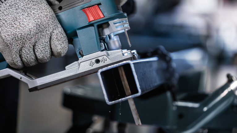 Orang yang mengenakan perlengkapan keselamatan menggunakan gergaji ukir untuk memotong balok logam.