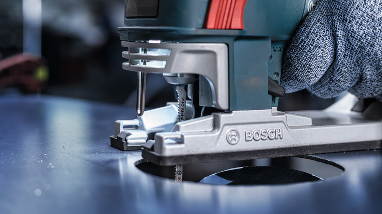 Orang yang mengenakan peralatan keselamatan memandu gergaji ukir untuk memotong lubang melingkar pada logam.