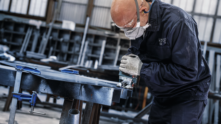 Orang yang mengenakan peralatan keselamatan menggunakan gergaji listrik untuk memotong logam di bengkel.