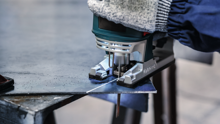 Seseorang yang mengenakan peralatan keselamatan memotong lembaran logam dengan gergaji ukir.