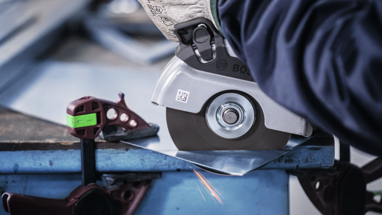 Orang yang mengenakan peralatan keselamatan memotong lembaran logam dengan penggiling sudut.