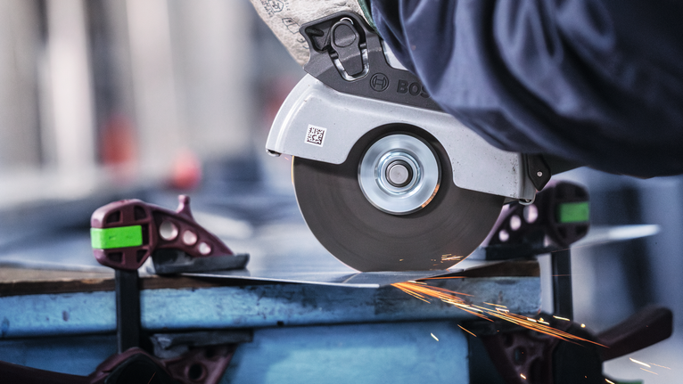 Orang yang mengenakan peralatan keselamatan memotong lembaran logam dengan gergaji bundar, menghasilkan percikan api.