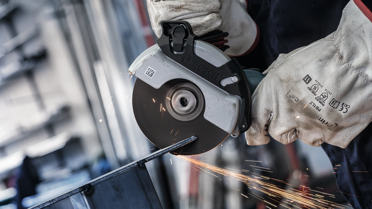 Orang yang mengenakan peralatan keselamatan menggunakan penggiling sudut untuk memotong logam, menghasilkan percikan api.