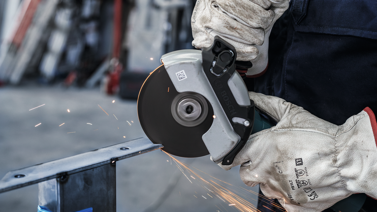 Seseorang yang mengenakan peralatan keselamatan memotong logam dengan gergaji bundar, sehingga menimbulkan percikan api.