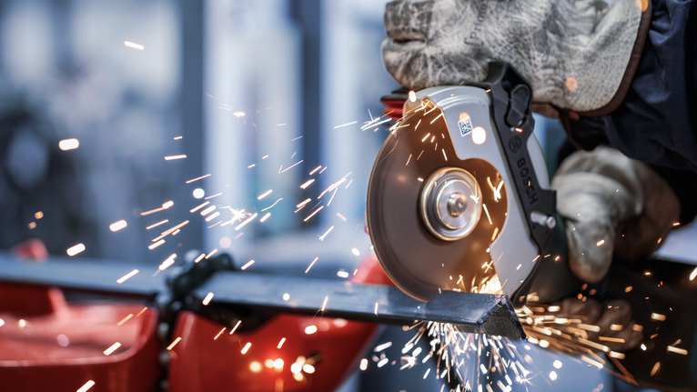 Orang yang mengenakan peralatan keselamatan menggunakan penggiling sudut untuk memotong logam, menghasilkan percikan api.