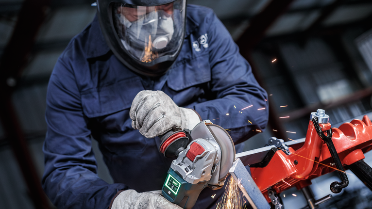 Seseorang yang mengenakan peralatan keselamatan menggiling logam, sehingga menimbulkan percikan api.