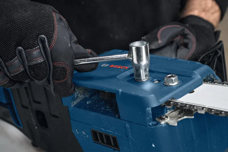 Seseorang yang mengenakan peralatan keselamatan menyetel gergaji mesin tanpa kabel dengan kunci pas.