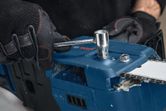 Seseorang yang mengenakan peralatan keselamatan menyetel gergaji mesin tanpa kabel dengan kunci pas.