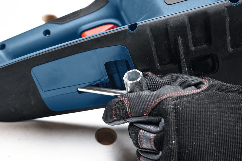 Seseorang yang mengenakan perlengkapan keselamatan menggunakan kunci pas untuk menyetel gergaji mesin tanpa kabel.