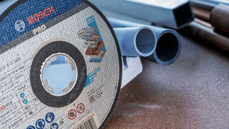 Cakram pemotong diletakkan di meja kerja di samping beberapa pipa plastik.