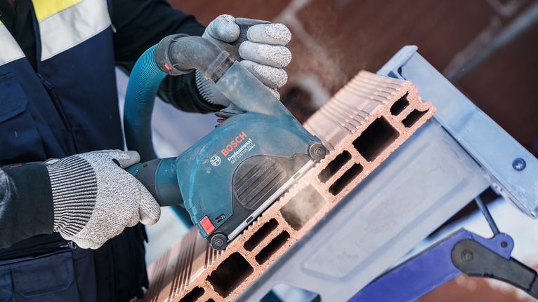 Seseorang yang mengenakan peralatan keselamatan memotong batu bata berongga dengan alat listrik.