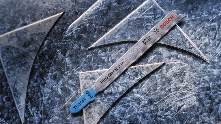 Mata gergaji ukir untuk memotong logam tipis diletakkan pada lembaran logam yang tergores.