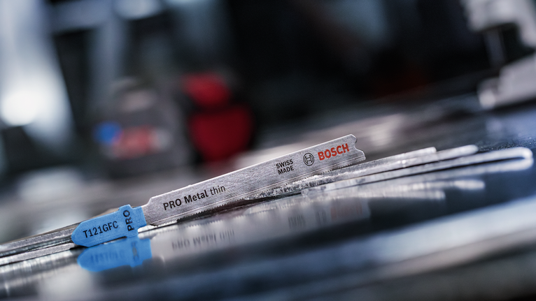 Mata gergaji ukir logam tergeletak pada permukaan logam reflektif di bengkel.