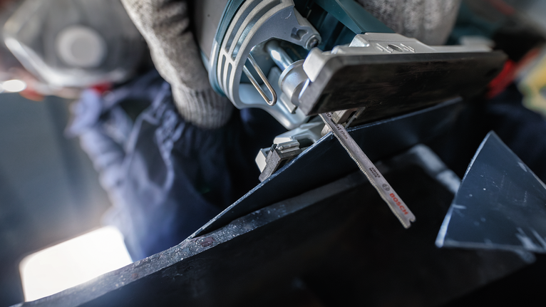 Orang yang mengenakan peralatan keselamatan memotong logam dengan gergaji ukir.