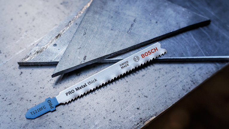 Mata gergaji logam diletakkan pada permukaan baja di samping lembaran logam yang dipotong.