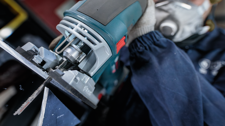 Orang yang mengenakan peralatan keselamatan menggunakan gergaji ukir untuk memotong logam.