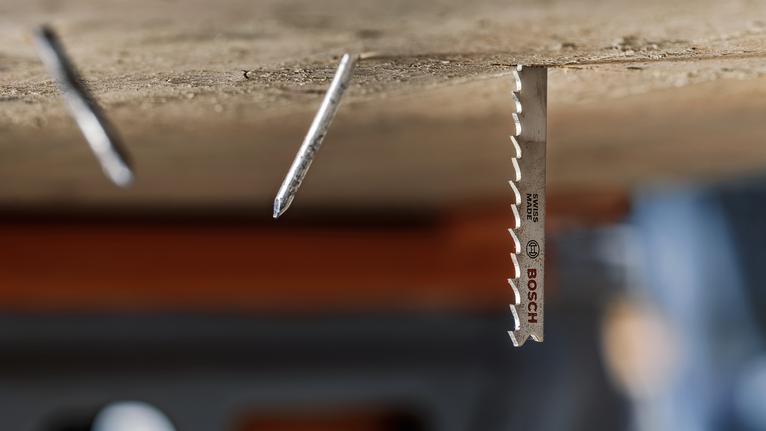 Mata gergaji logam yang dipasang di kayu di samping dua paku yang menonjol.