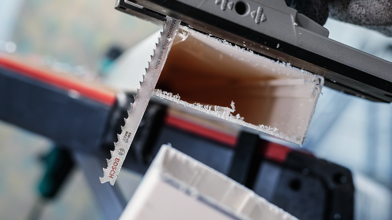 Seseorang yang mengenakan peralatan keselamatan memotong pipa plastik dengan mata gergaji ukir.