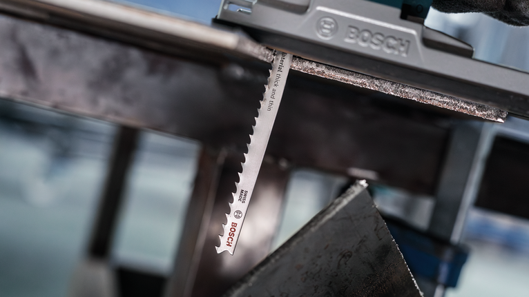 Orang yang mengenakan perlengkapan keselamatan menggunakan gergaji ukir untuk memotong lembaran logam.