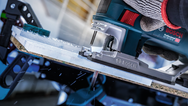 Orang yang mengenakan peralatan keselamatan memotong lembaran plastik dengan gergaji ukir.