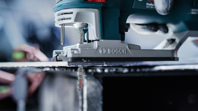 Seseorang yang mengenakan peralatan keselamatan memandu gergaji ukir untuk memotong lembaran logam.