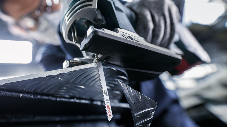 Seseorang yang mengenakan peralatan keselamatan memotong logam berpola dengan gergaji ukir.