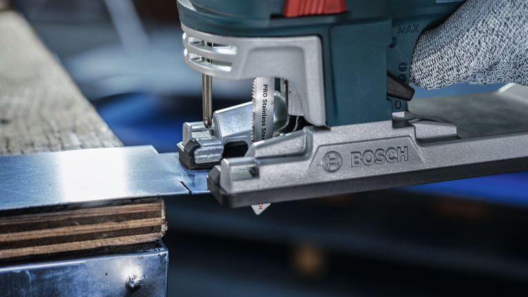 Orang yang mengenakan peralatan keselamatan memotong lembaran logam dengan gergaji ukir.