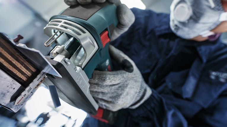 Seseorang yang mengenakan perlengkapan keselamatan mengoperasikan perkakas listrik untuk memotong sepotong logam.