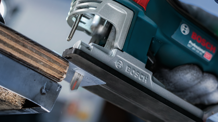 Seseorang yang mengenakan perlengkapan keselamatan menggunakan gergaji ukir untuk memotong kayu.