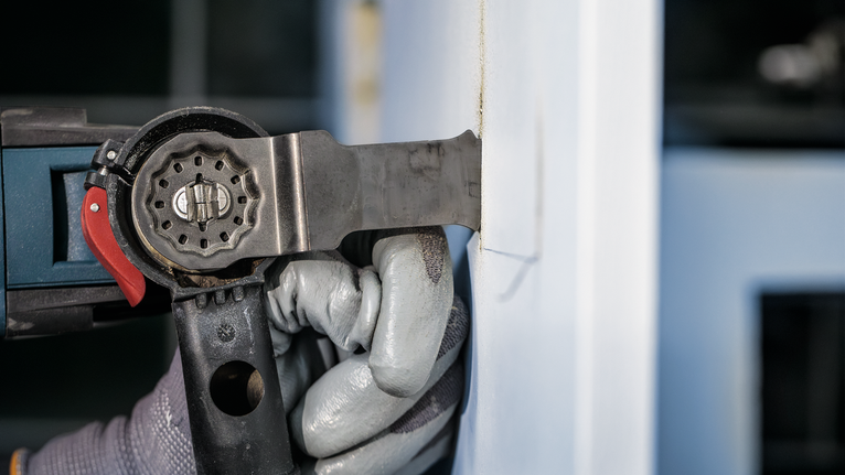 Orang yang mengenakan peralatan keselamatan menggunakan alat listrik untuk memotong dinding.