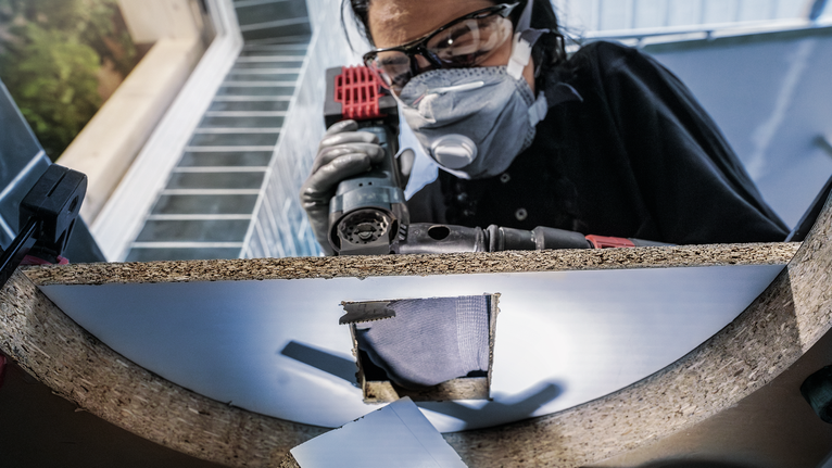 Orang yang mengenakan peralatan keselamatan mengebor lubang di papan kayu.