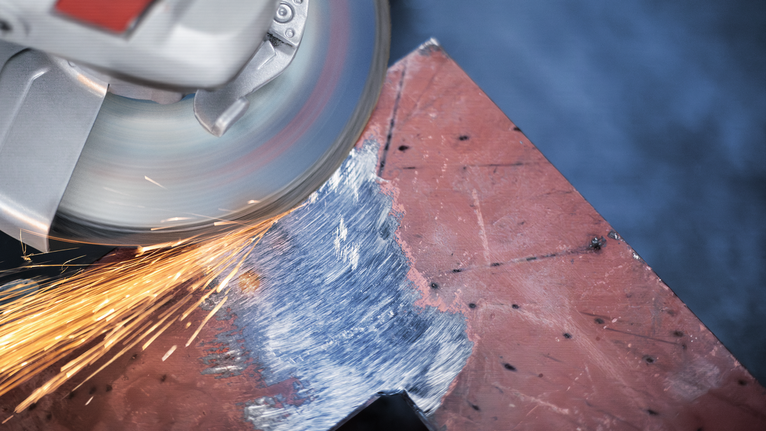 Penggiling sudut menghasilkan percikan api saat mengampelas tepi lembaran logam.
