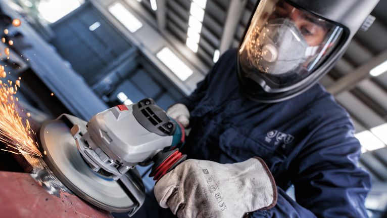 Seseorang yang mengenakan peralatan keselamatan menggiling logam, yang menyebabkan percikan api beterbangan.