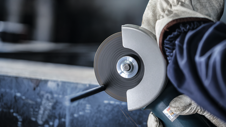 Orang yang mengenakan peralatan keselamatan menggunakan penggiling sudut untuk memotong logam.