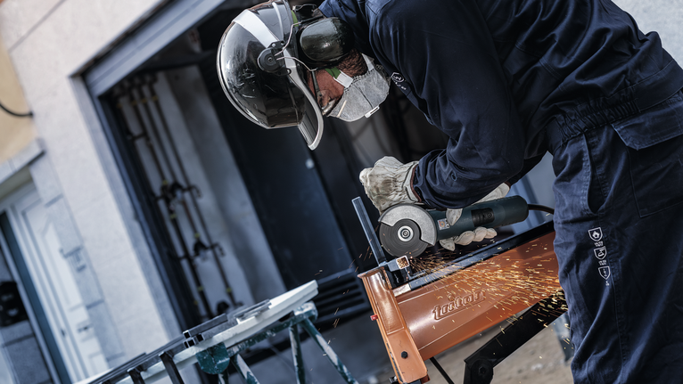 Seseorang yang mengenakan peralatan keselamatan menggiling logam, sehingga menimbulkan percikan api.