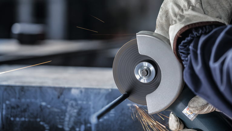 Orang yang mengenakan peralatan keselamatan memotong logam dengan penggiling sudut, sehingga menimbulkan percikan api.