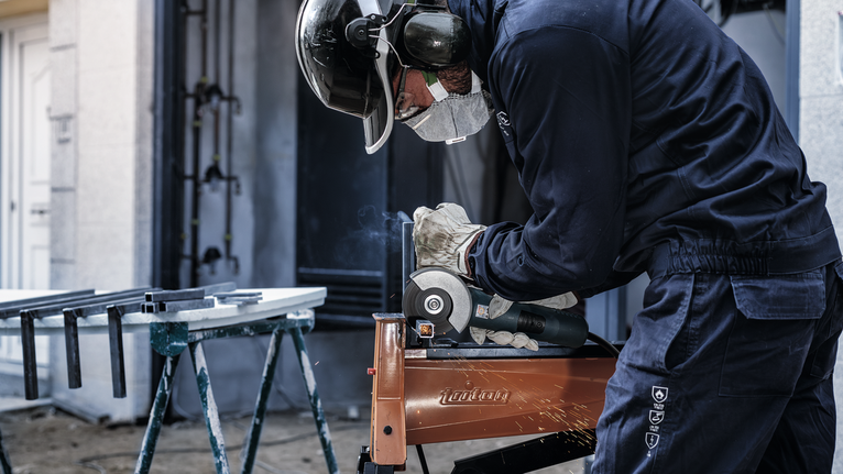 Seseorang yang mengenakan peralatan keselamatan menggiling logam, sehingga menimbulkan percikan api.