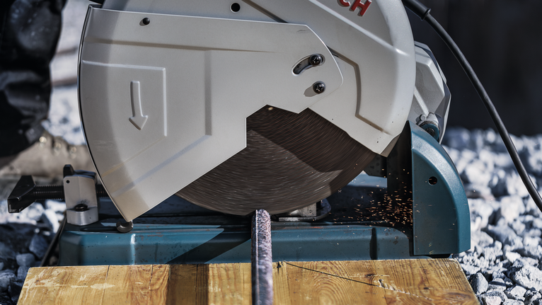 Gergaji pemotong logam yang mengiris tulangan, menghasilkan percikan api pada permukaan kayu.