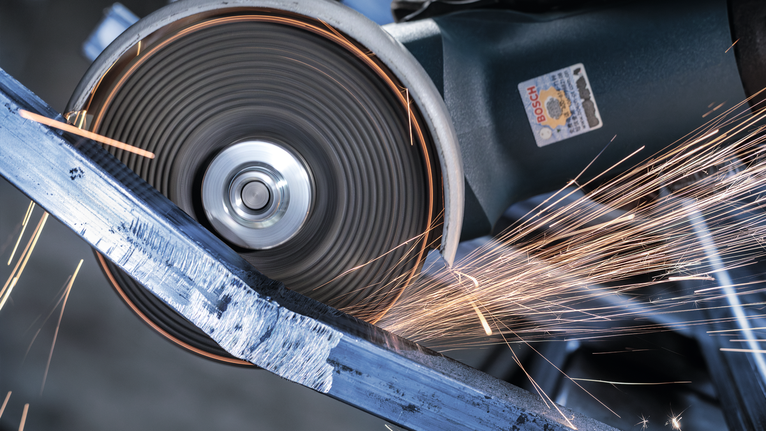 Roda pemotong mengiris balok logam, menghasilkan percikan terang.