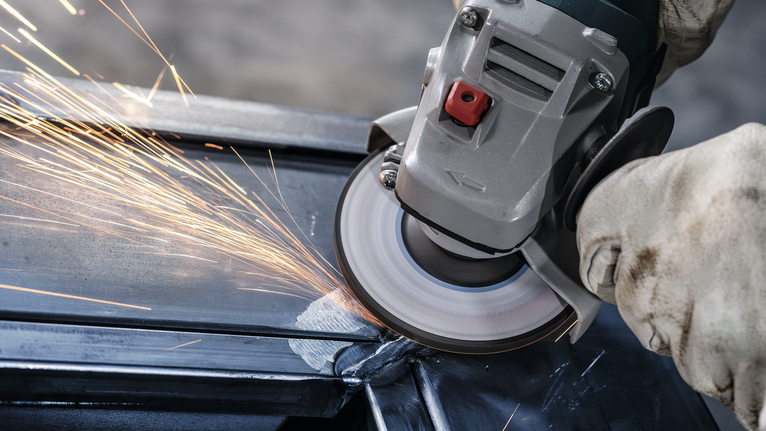 Orang yang mengenakan peralatan keselamatan menggiling logam, menghasilkan percikan terang.