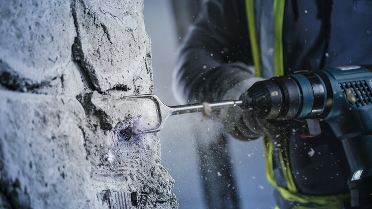 Seseorang yang mengenakan perlengkapan keselamatan menggunakan palu putar untuk memecahkan beton.