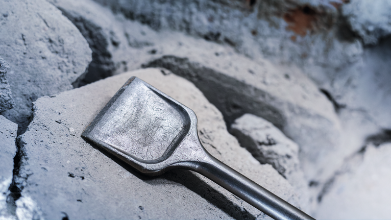 Pahat lebar bertumpu pada puing beton yang pecah.