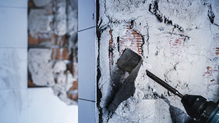 Palu pembongkaran mengelupas plester dari dinding bata.