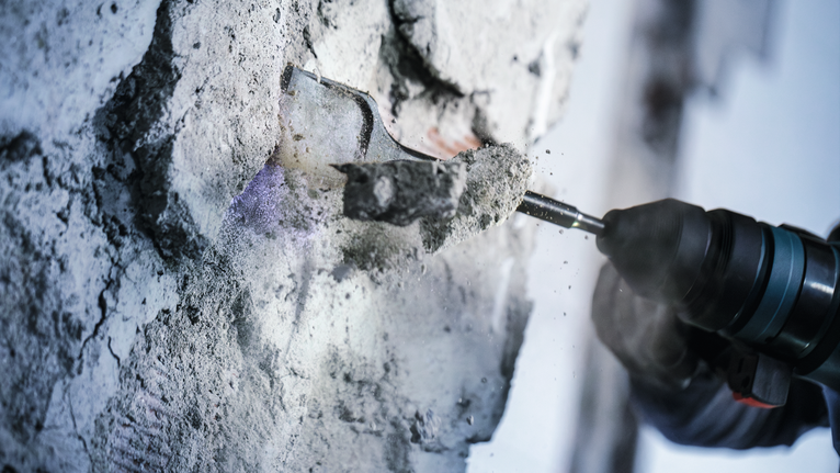 Orang yang mengenakan peralatan keselamatan memahat beton dari dinding dengan palu putar.
