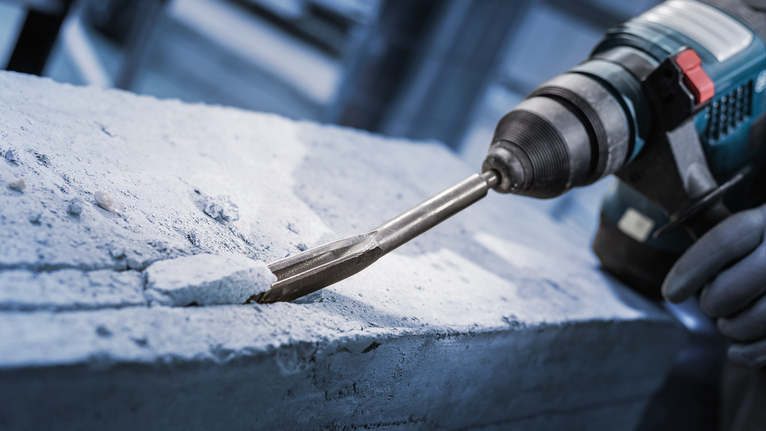 Chisel PRO SDS plus Hollow Gouging, 22 x 250 mm Orang yang mengenakan peralatan keselamatan sedang memahat beton dengan palu putar.