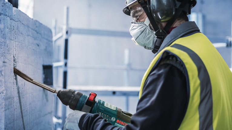 Chisel PRO SDS plus Hollow Gouging, 22 x 250 mm Orang yang mengenakan peralatan keselamatan sedang memahat beton dengan alat listrik.