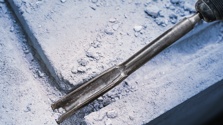Chisel PRO SDS plus Hollow Gouging, 22 x 250 mm Alat pahat memecah beton dengan debu dan serpihan berserakan di sekitarnya.
