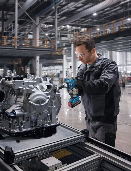 Seseorang yang mengenakan perlengkapan keselamatan menggunakan kunci pas benturan tanpa kabel pada rakitan mesin.