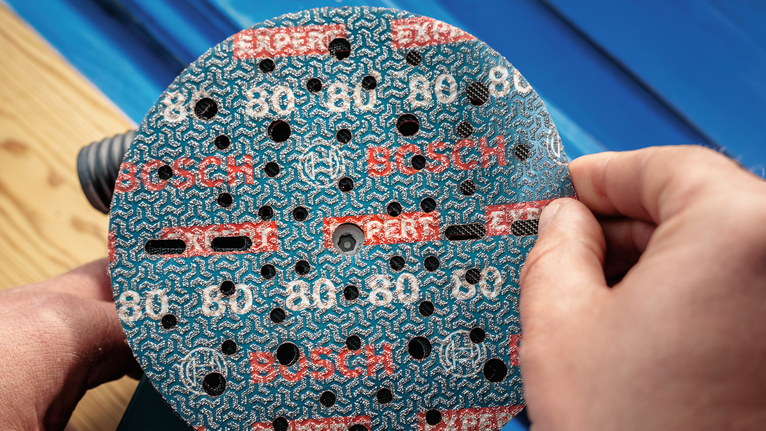 Orang yang memasang cakram pengamplas pada mesin pengamplas listrik.